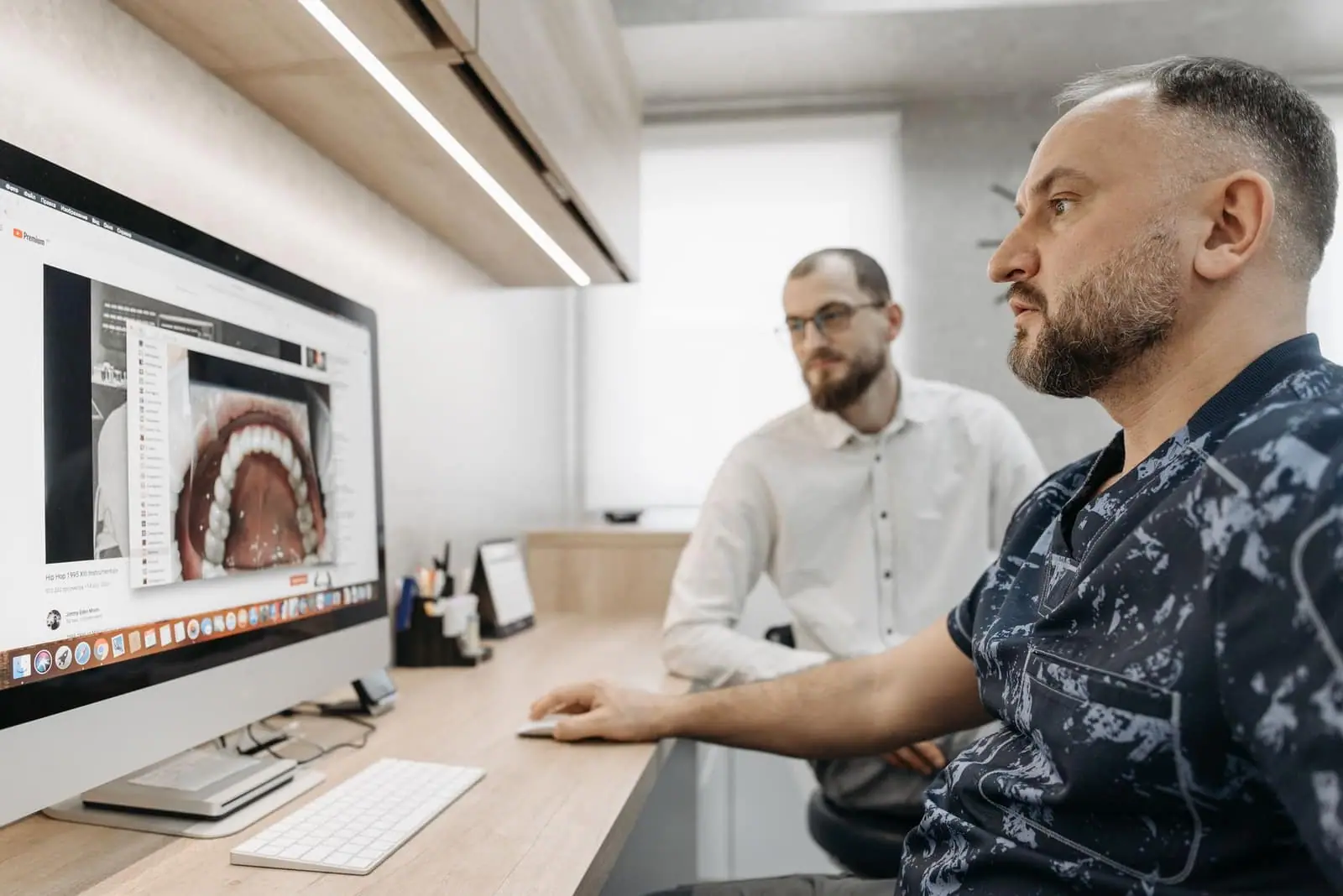 Two men discuss dental care at a computer, illustrating modern digital dentistry.