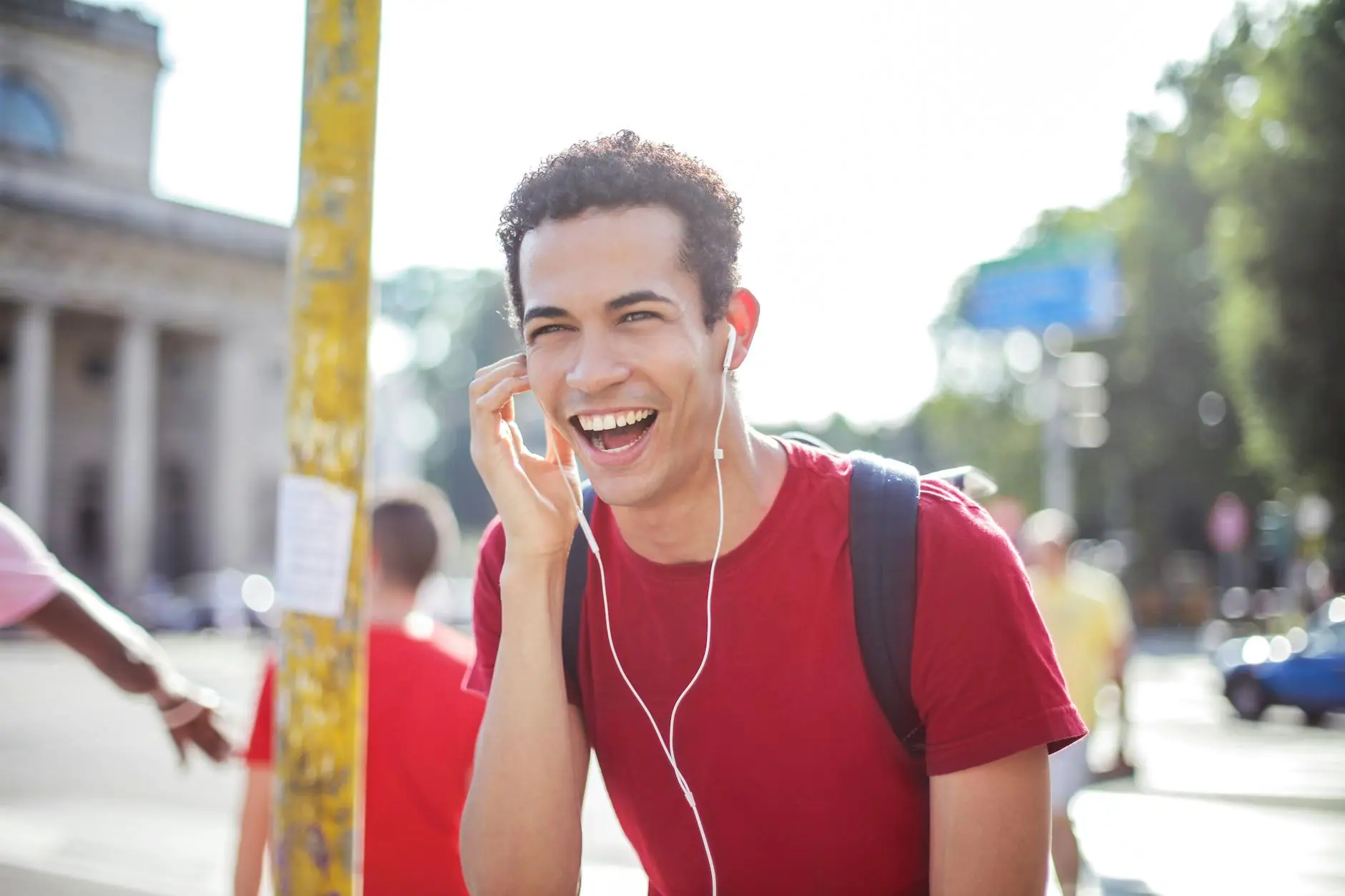 Young man enjoying music through headphones, smiling brightly under the sun.